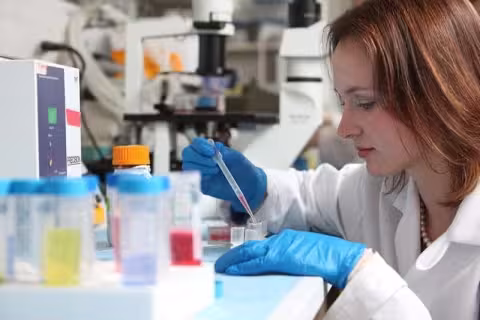 Researcher using a pipette to transfer liquid samples in a laboratory with scientific equipment and test tubes.