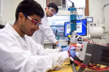 Student working with laboratory equipment in a chemical engineering research lab while another student conducts an experiment in the background.